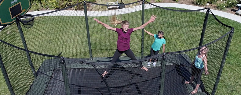 Girl on trampoline with two other girls watching. All backyard trampolines sold at Swingset Warehouse have safety netting.