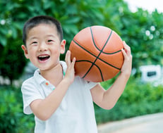 Small Asian boy with basketball. Make sure your basketball system has an adjustable pole so your system can grow with your family.
