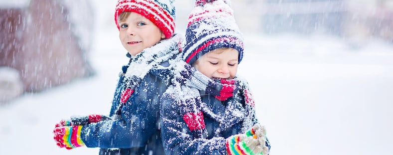 Kids standing in the snow with colorful striped gloves.